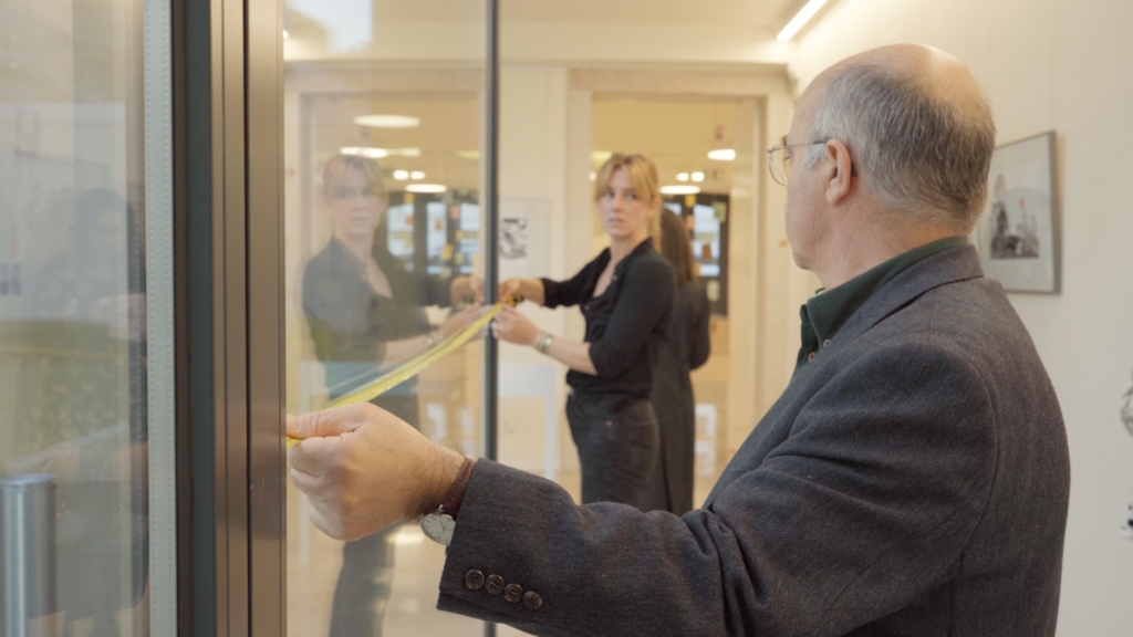 Duas pessoas no corredor a medir um vidro com uma fita métrica