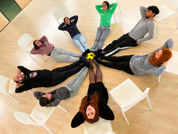 Foto a cores de 8 pessoas, deitadas, a formarem um círculo.