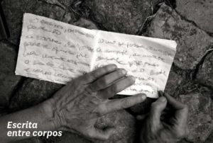 Fotografia a preto e branco de duas mãos de uma pessoa a escrever num guardanapo de papel. Foto da autoria de Valentina Parravicini.