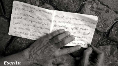 Fotografia a preto e branco de duas mãos de uma pessoa a escrever num guardanapo de papel. Foto da autoria de Valentina Parravicini.