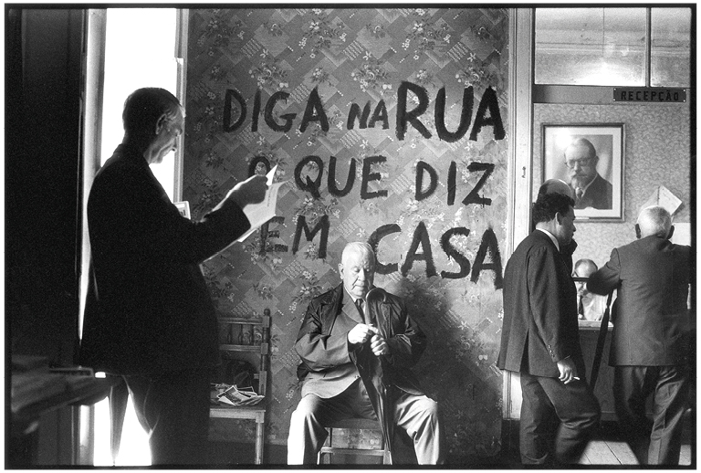 Fotografia de Carlos Gil, a preto e branco, onde se lê a frase "Diga na rua o que se diz em casa".