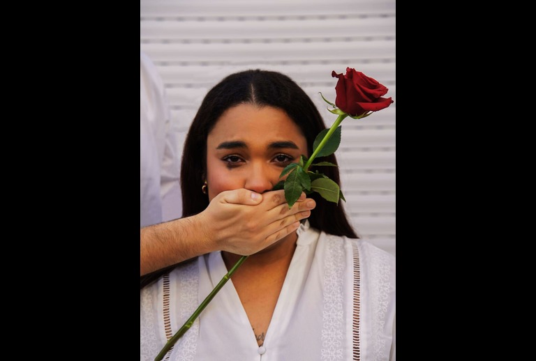 Imagem de uma mulher com uma mão masculina a tapar-lhe a boca.