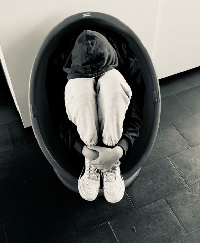 Imagem de uma pessoa jovem, sentada no chão, encolhida e com a cara escondida, pousada nos joelhos.