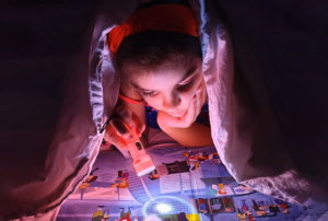 Imagem de uma criança a ler no escuro com uma lanterna.