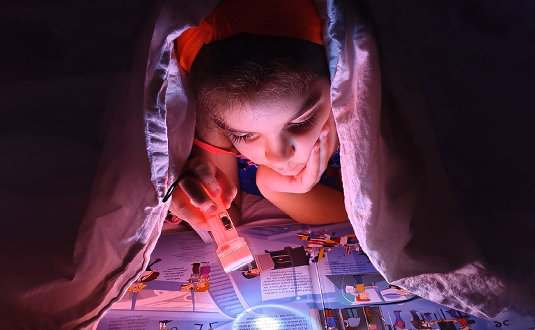 Imagem de uma criança a ler no escuro com uma lanterna.