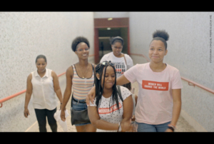 Imagem com cinco mulheres a caminhar num corredor.