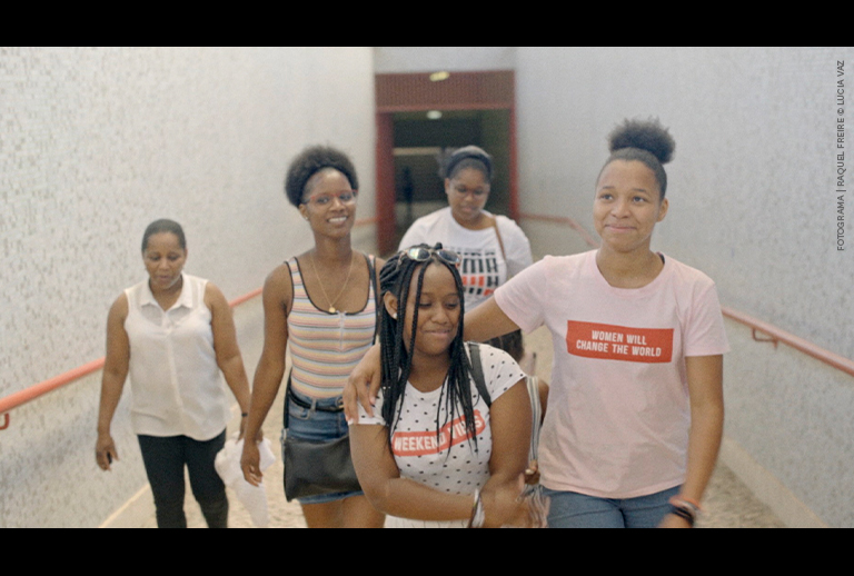 Imagem com cinco mulheres a caminhar num corredor.