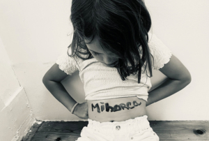 Imagem com uma foto de uma criança , de cabeça baixa, e está escrito na sua barriga a palavra 'minorca'.