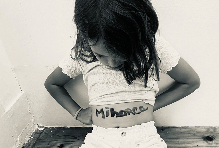 Imagem com uma foto de uma criança , de cabeça baixa, e está escrito na sua barriga a palavra 'minorca'.